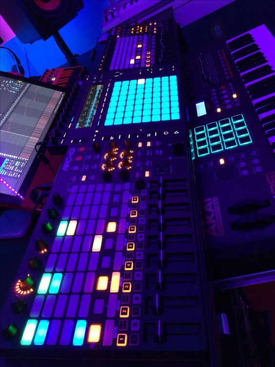 Neon-lit electronic music controller with glowing blue and purple pads and buttons in a dark studio