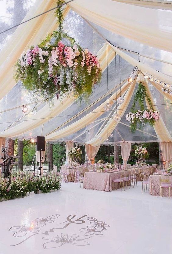Elegant outdoor wedding tent with white drapes, hanging floral arrangement, and pastel table settings