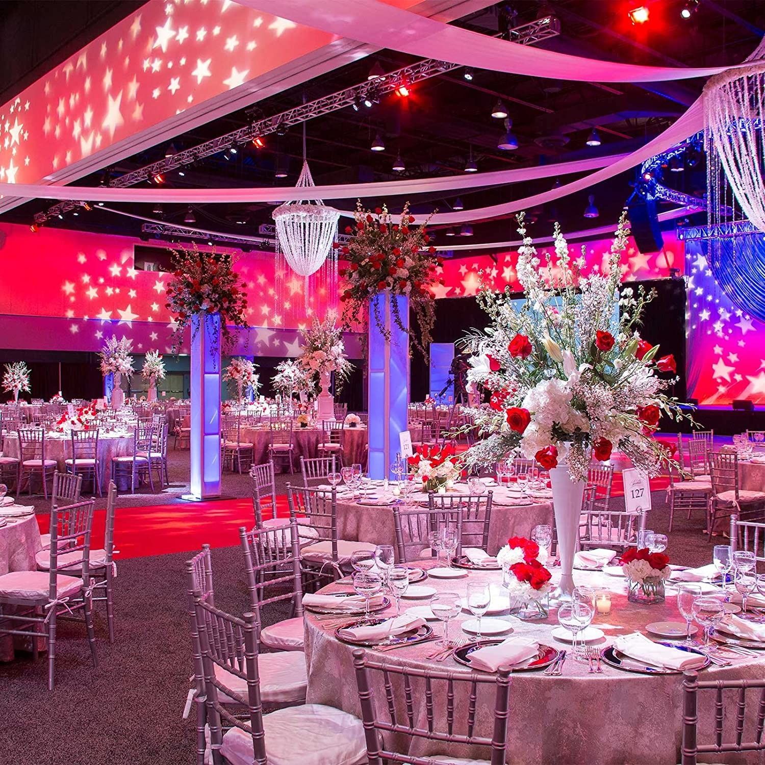 Elegant banquet hall with pink lighting, star projections, and decorated tables set for an event
