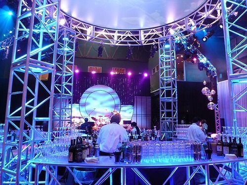 Blue-lit stage setup with truss lighting, DJ equipment, and staff in a nightclub or event venue