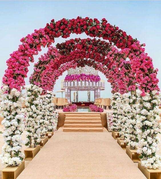 Flower-lined wedding aisle with pink and white arches leading to a decorated stage outdoors