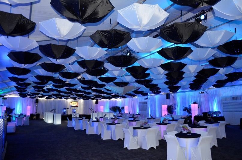 Modern banquet hall with white tables, blue lighting, and a geometric black-and-white ceiling decoration