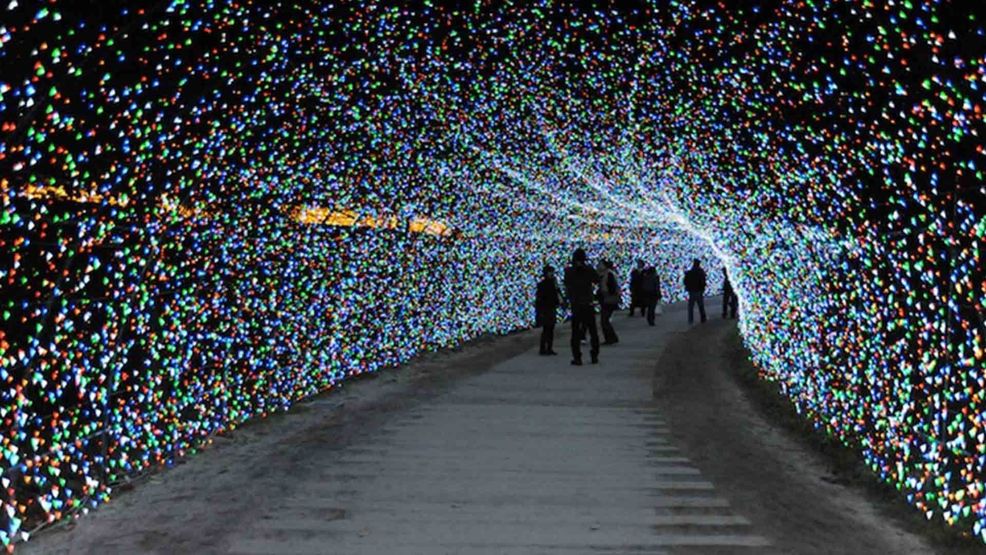 People walking through a colorful light tunnel over a pathway at night