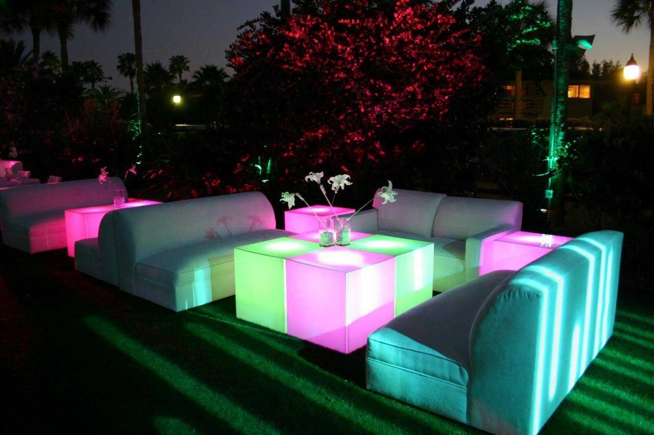 Glowing neon lounge furniture arranged outdoors at night, lit in pink, green, and blue.