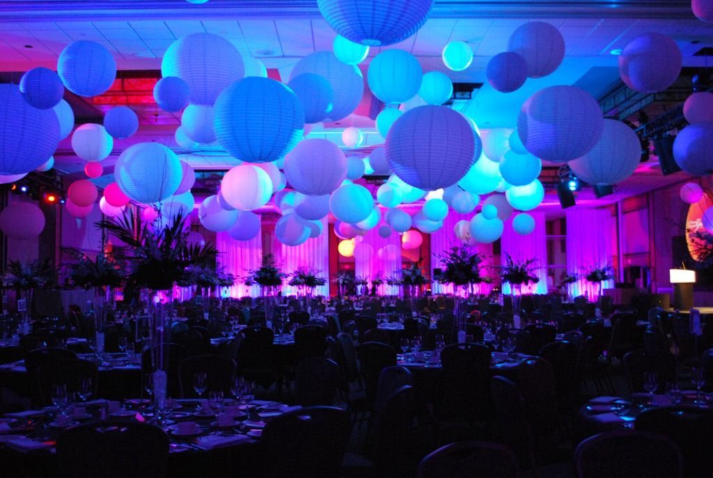Colorful indoor event hall with glowing blue and pink hanging lanterns above tables and guests