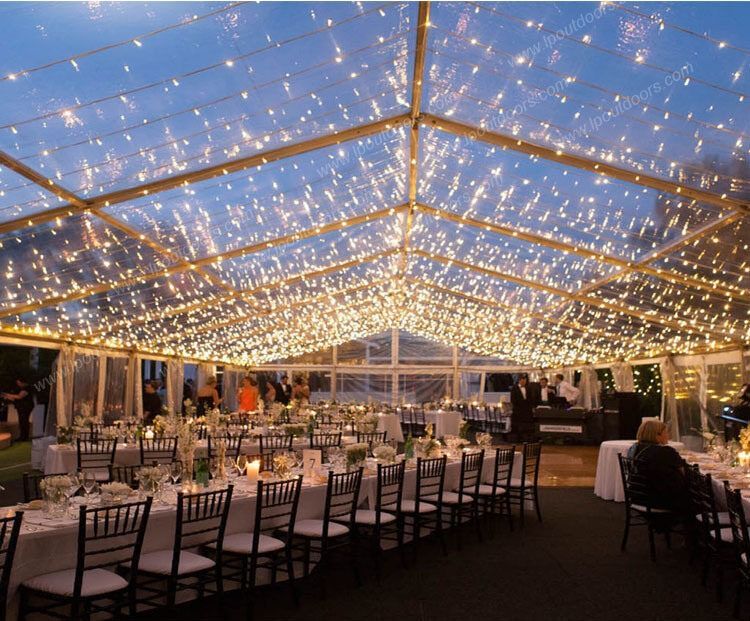 Elegant outdoor reception tent with warm string lights and rows of white-draped tables and chairs at dusk