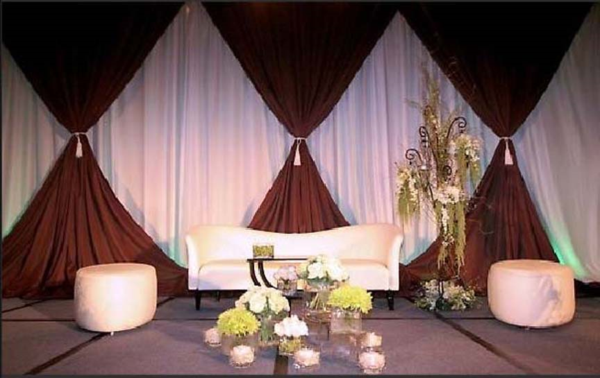Elegant event stage with white sofa, dark drapes, floral arrangement, and soft pink lighting