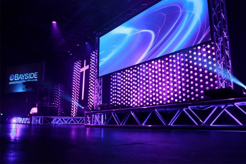 Purple-lit stage with large LED screen and “BAYSIDE” sign in an empty concert venue
