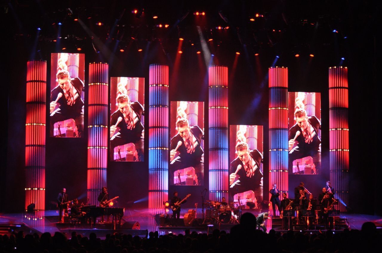 Concert stage with tall red LED screens showing performers and a band below