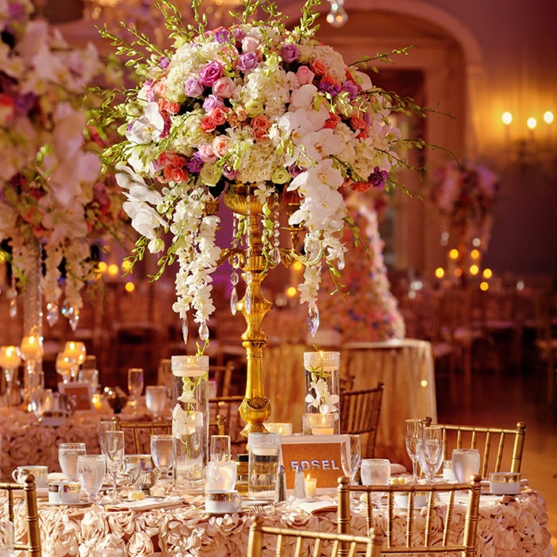 Elegant banquet table with a tall pink and white floral centerpiece in a warmly lit reception hall