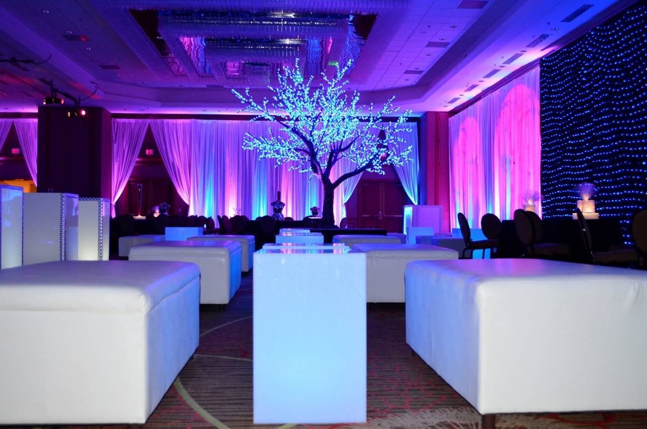 Elegant lounge with white seating, purple-blue uplighting, and a glowing decorative tree centerpiece