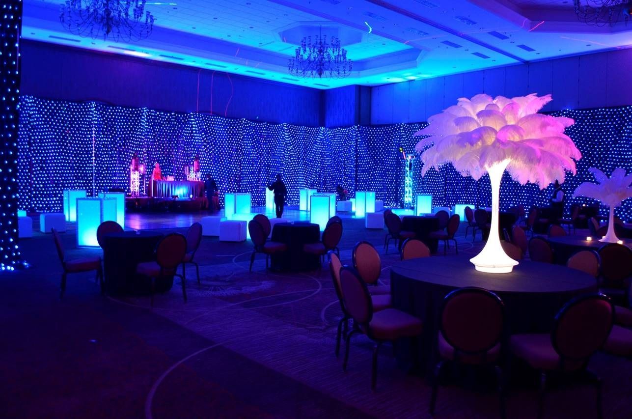 Blue-lit banquet hall with round tables and a glowing white tree centerpiece