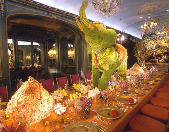 Elegant banquet table with flowers, chandeliers, and a green parrot centerpiece in a grand dining room