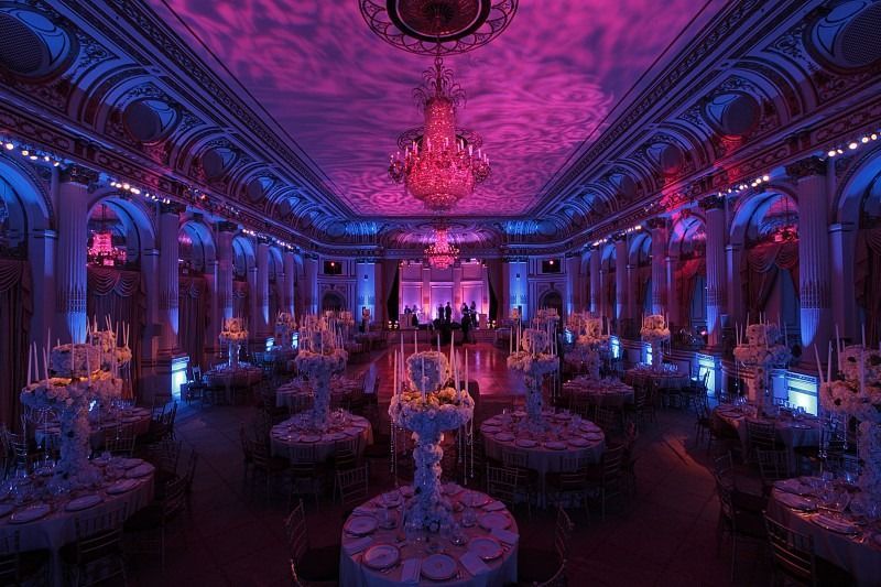 Lavishly lit banquet hall with ornate ceiling, purple and pink lighting, and round tables set for an event