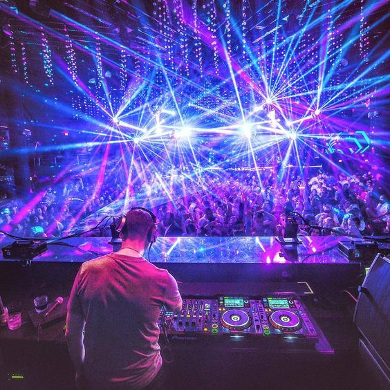 DJ mixing in a neon-lit club, with purple-blue laser lights over a packed crowd