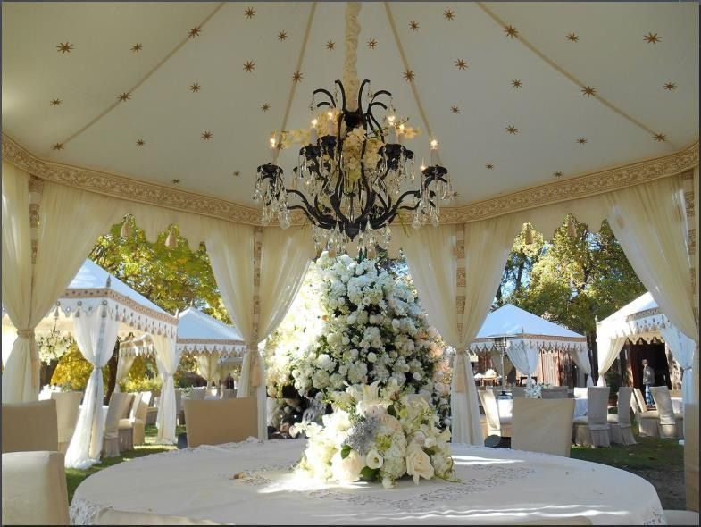 Elegant white floral display under a cream tent with a chandelier and draped curtains outdoors