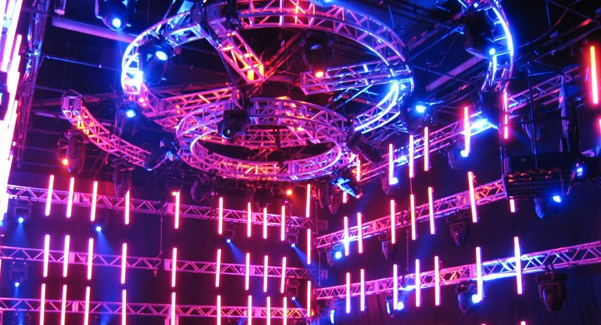 Neon-lit concert stage with pink and blue lights and a circular overhead display in a dark venue