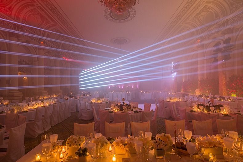 Elegant banquet hall with round tables, warm candlelight, and pink laser beams across the ceiling