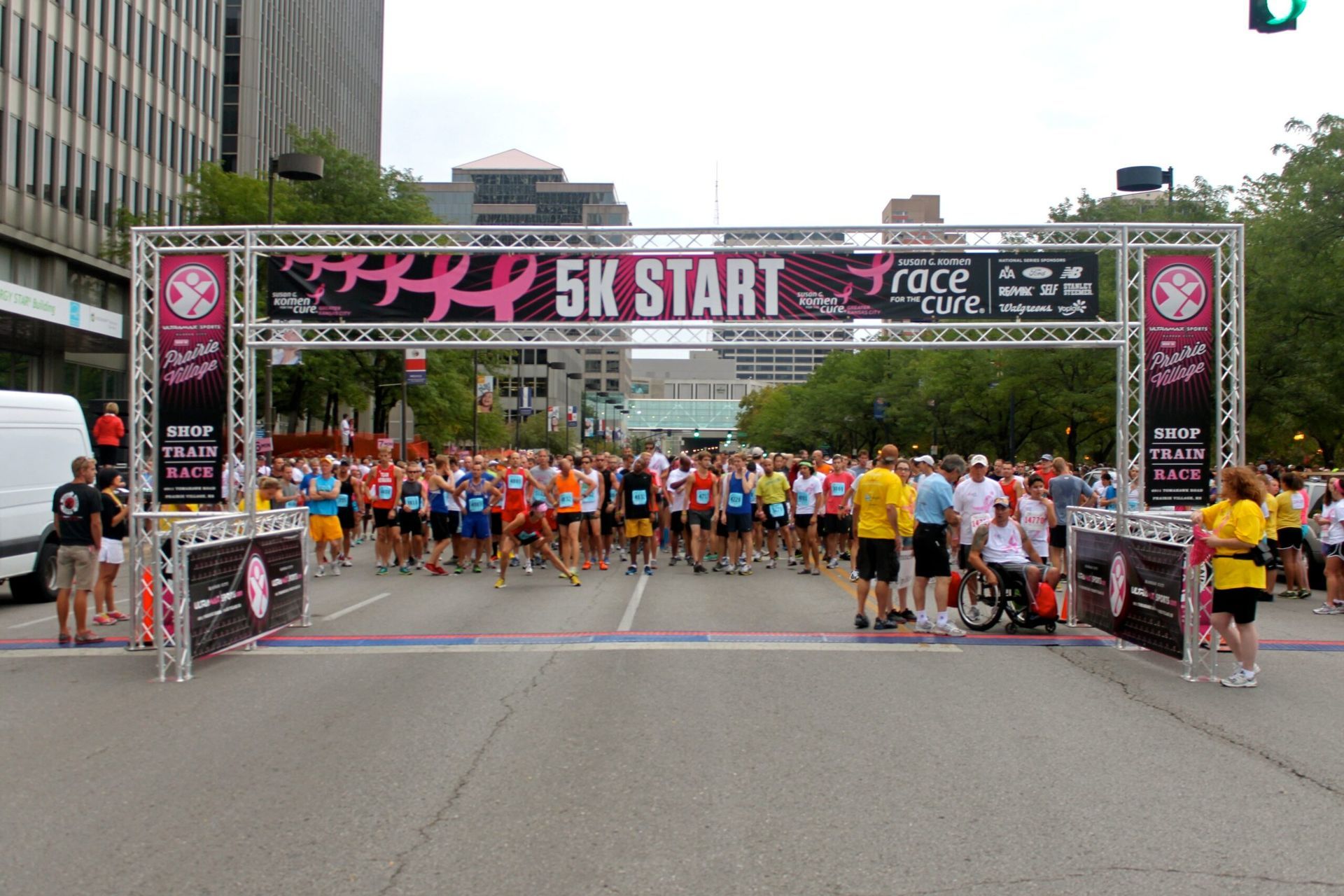 Runners gathered at the start line under a pink 5K START arch in a city street race.