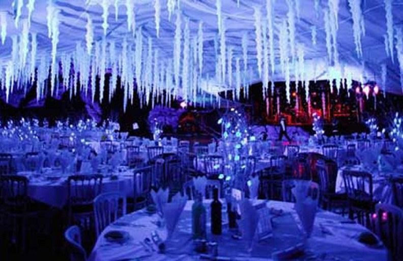 Blue-lit banquet hall with icicle decorations, set tables, and chairs under hanging lights