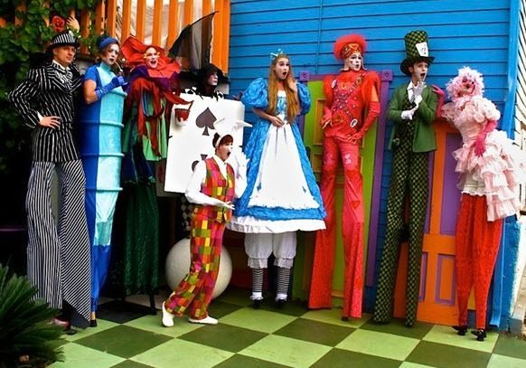 Colorful group of people in whimsical costumes posing against a striped wall and checkered floor