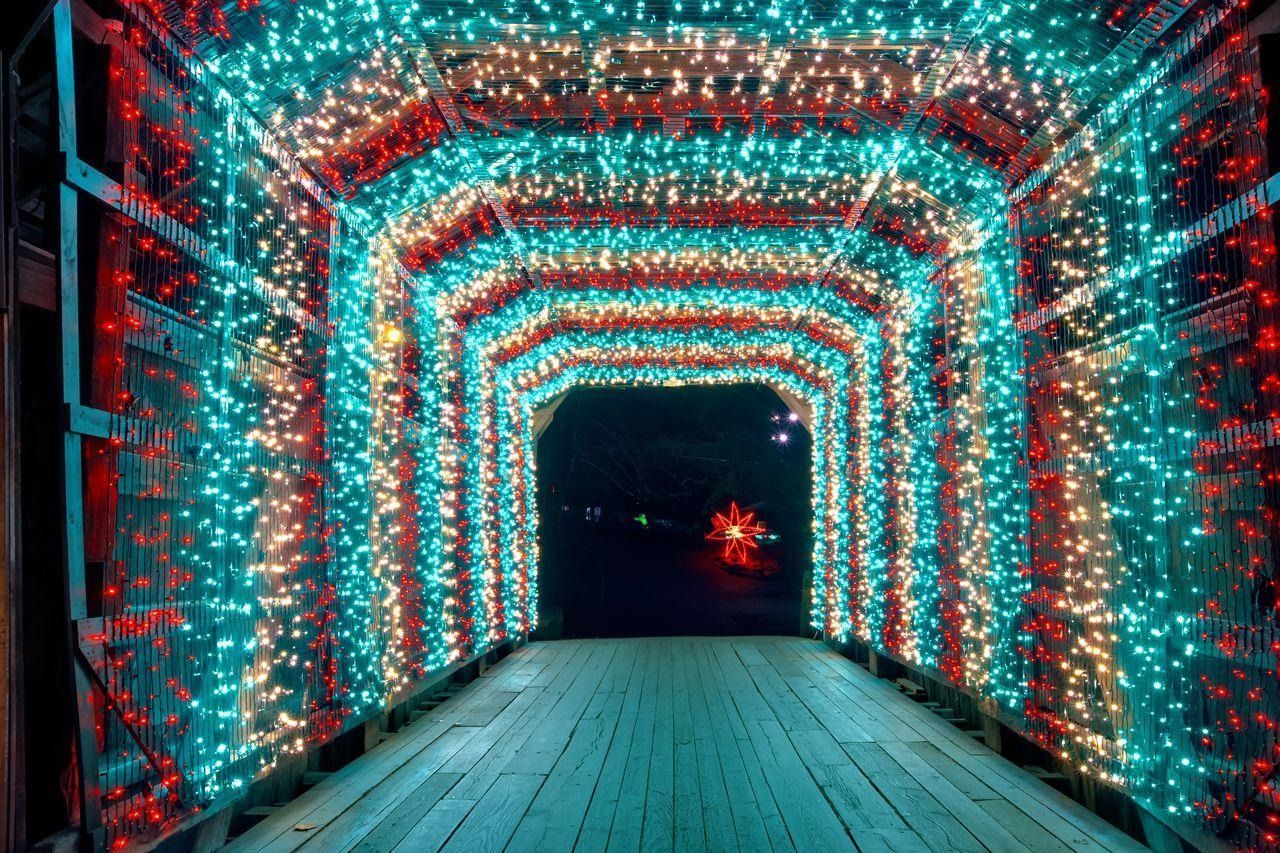 A glowing tunnel of red, blue, and white lights over a wooden walkway at night