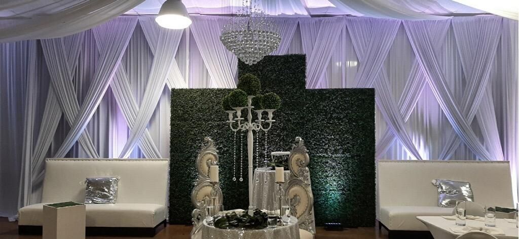 Elegant event display with white draped backdrop, purple lighting, and a floral centerpiece on a black panel