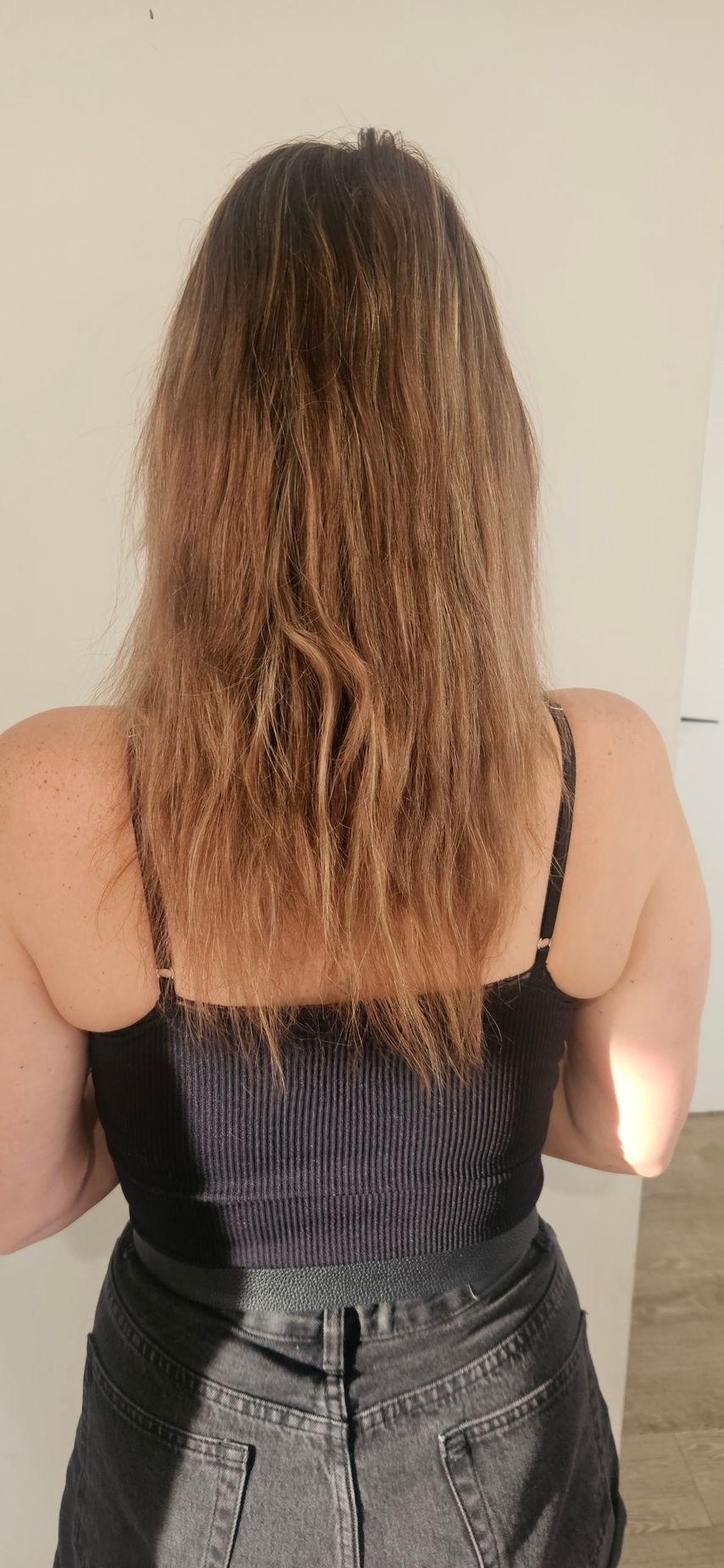 Woman facing away, with long, frizzy brown hair. Wearing a black tank top and denim skirt.