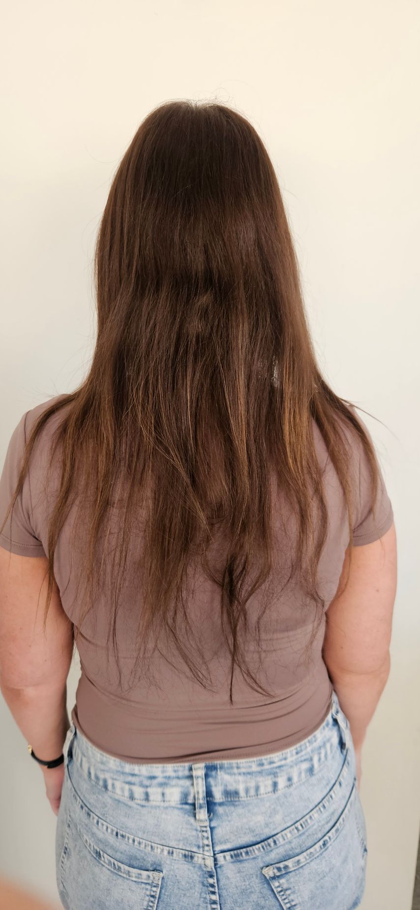 Person wearing a brown shirt and blue jeans with long brown hair from the back.