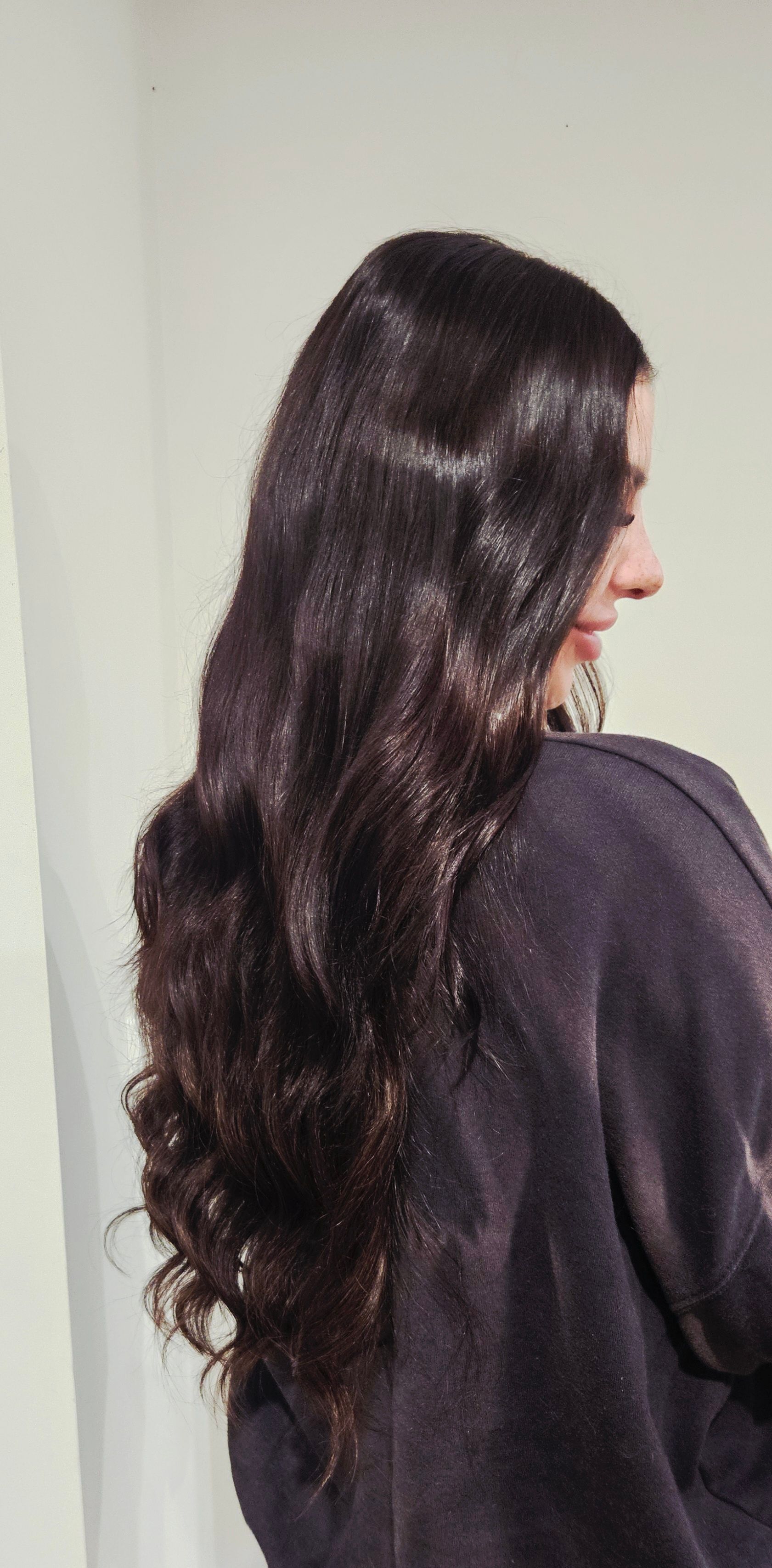 Woman with long, dark, wavy hair, wearing a dark sweater, in a neutral setting.