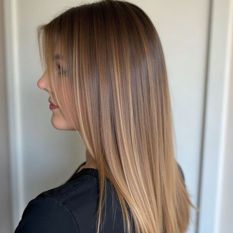 Woman with long, straight brown hair with blonde highlights, wearing a black top, looking to the side.