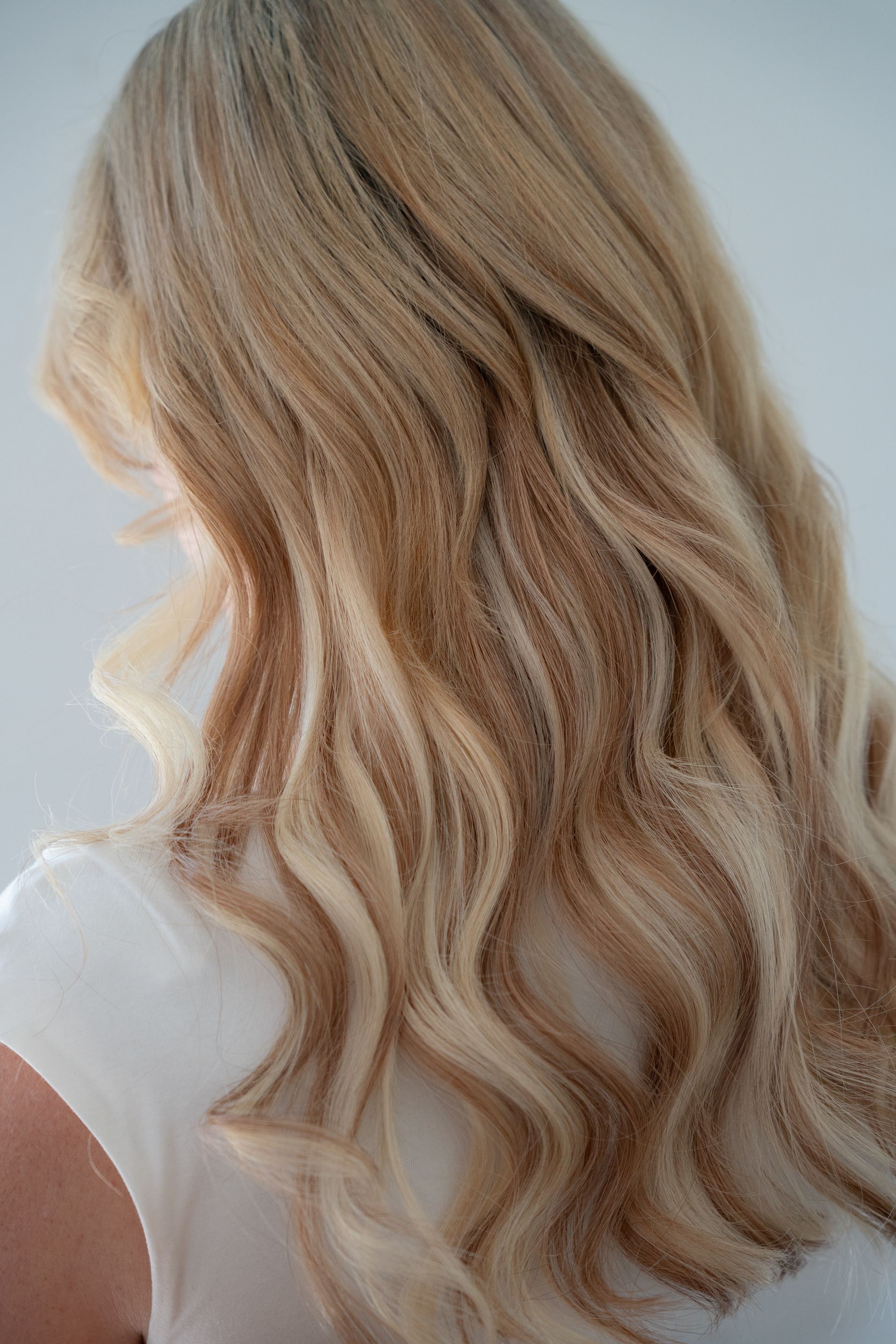 Blonde hair with light brown highlights cascading over a white shirt.