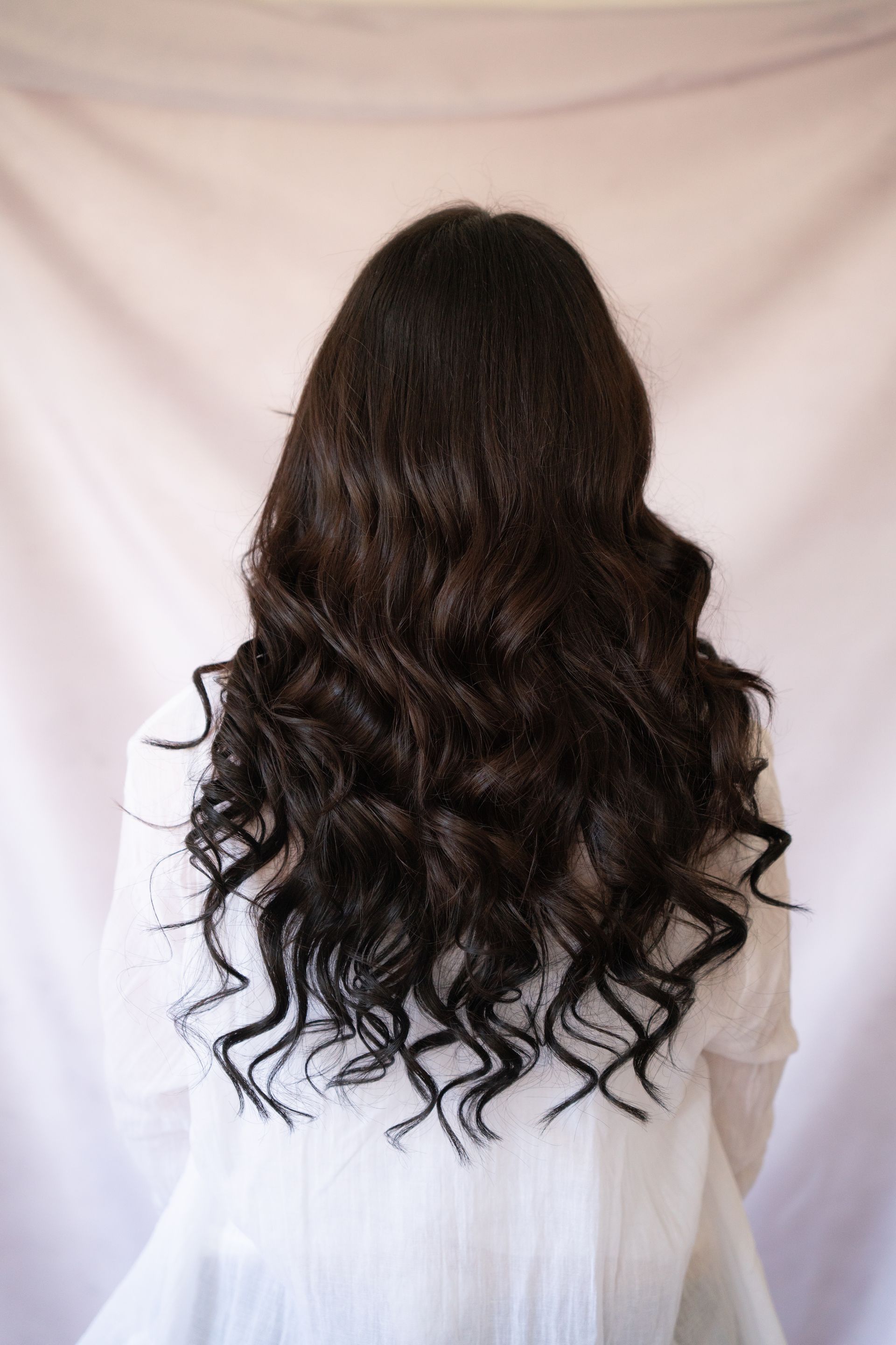 Person with long, dark, curly hair wearing a white shirt, back to camera.