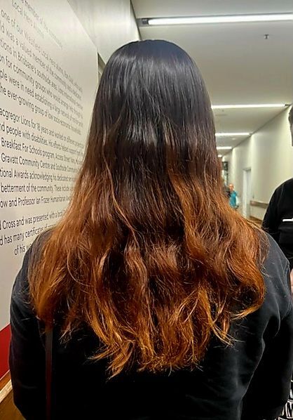 Woman with dark hair fading into a warm brown ombre, standing in a hallway.