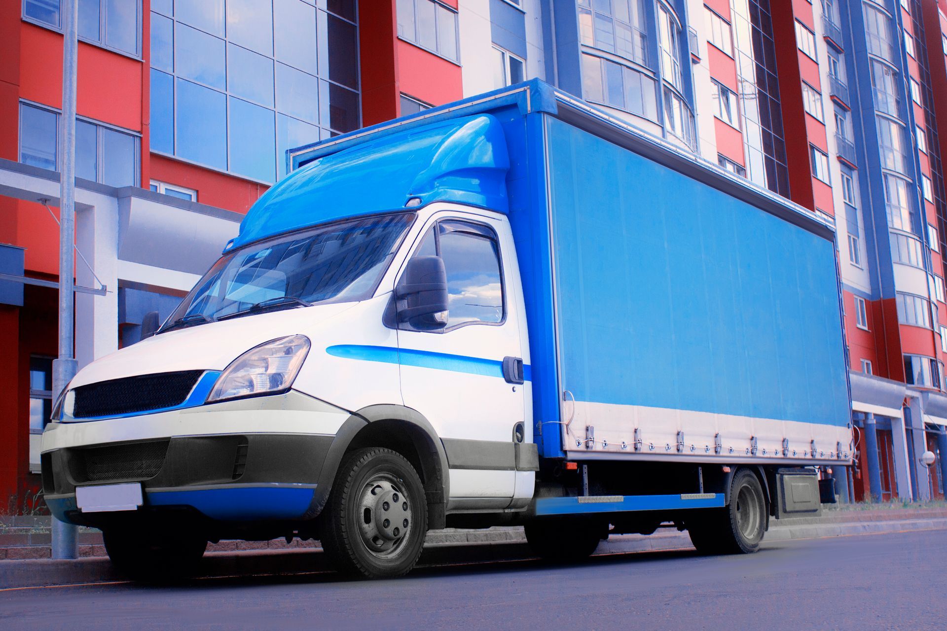 Blue and white interstate movers truck parked outside a modern apartment building.