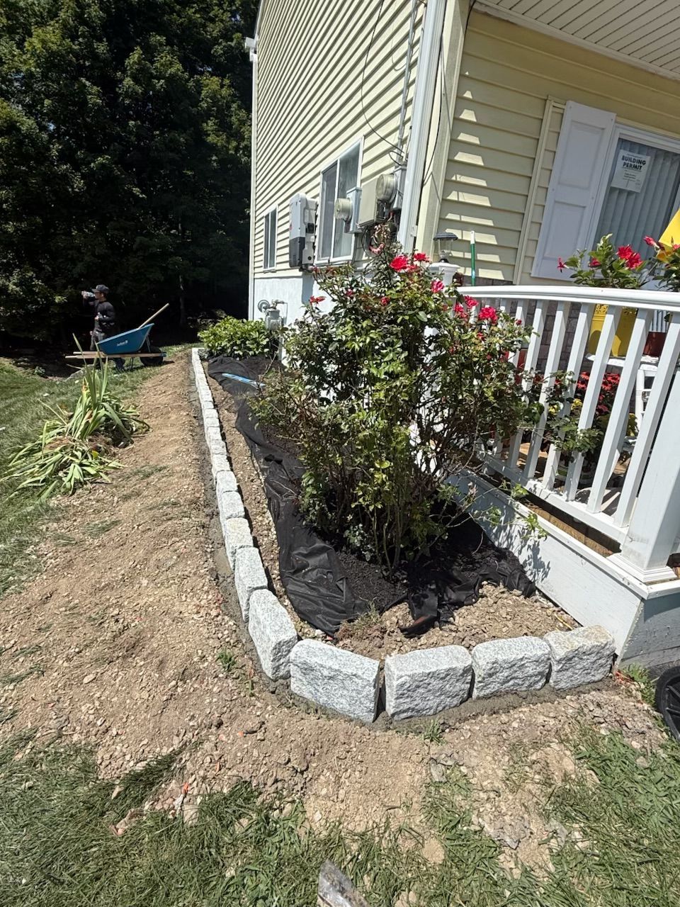 A house with a flower bed outlined by gray blocks, roses, and black mulch.