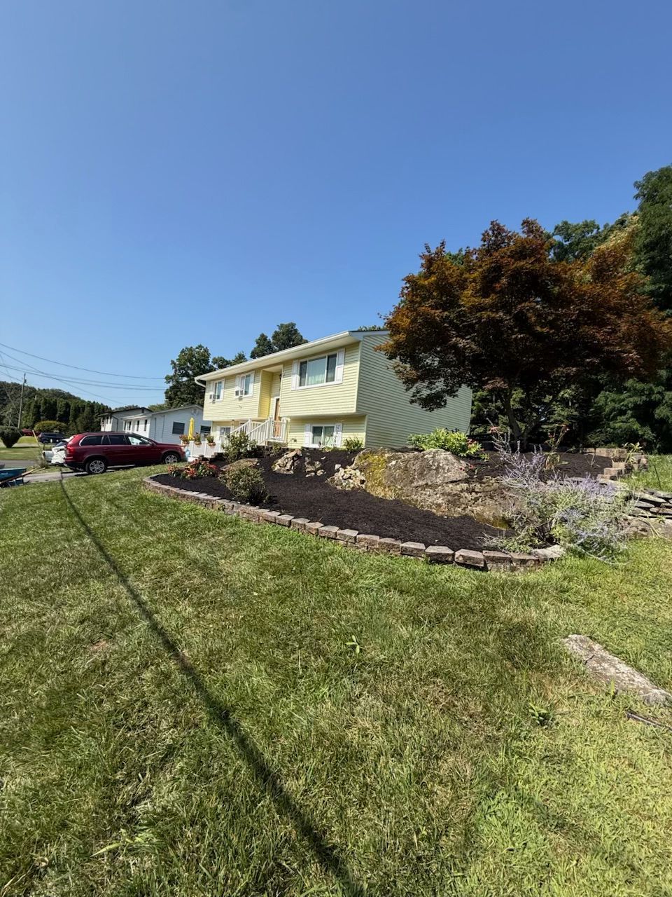 Yellow house with landscaping and red car on a sunny day.