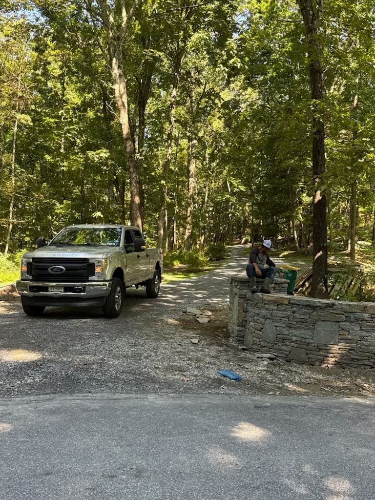 A silver pickup truck parked near a stone wall and a person in the woods.