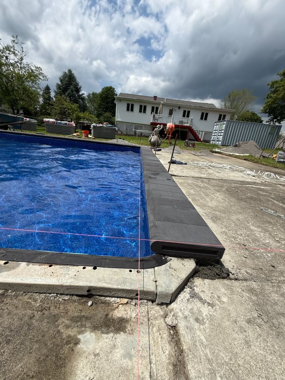 Pool under construction with a blue liner, dark coping, and concrete surround.