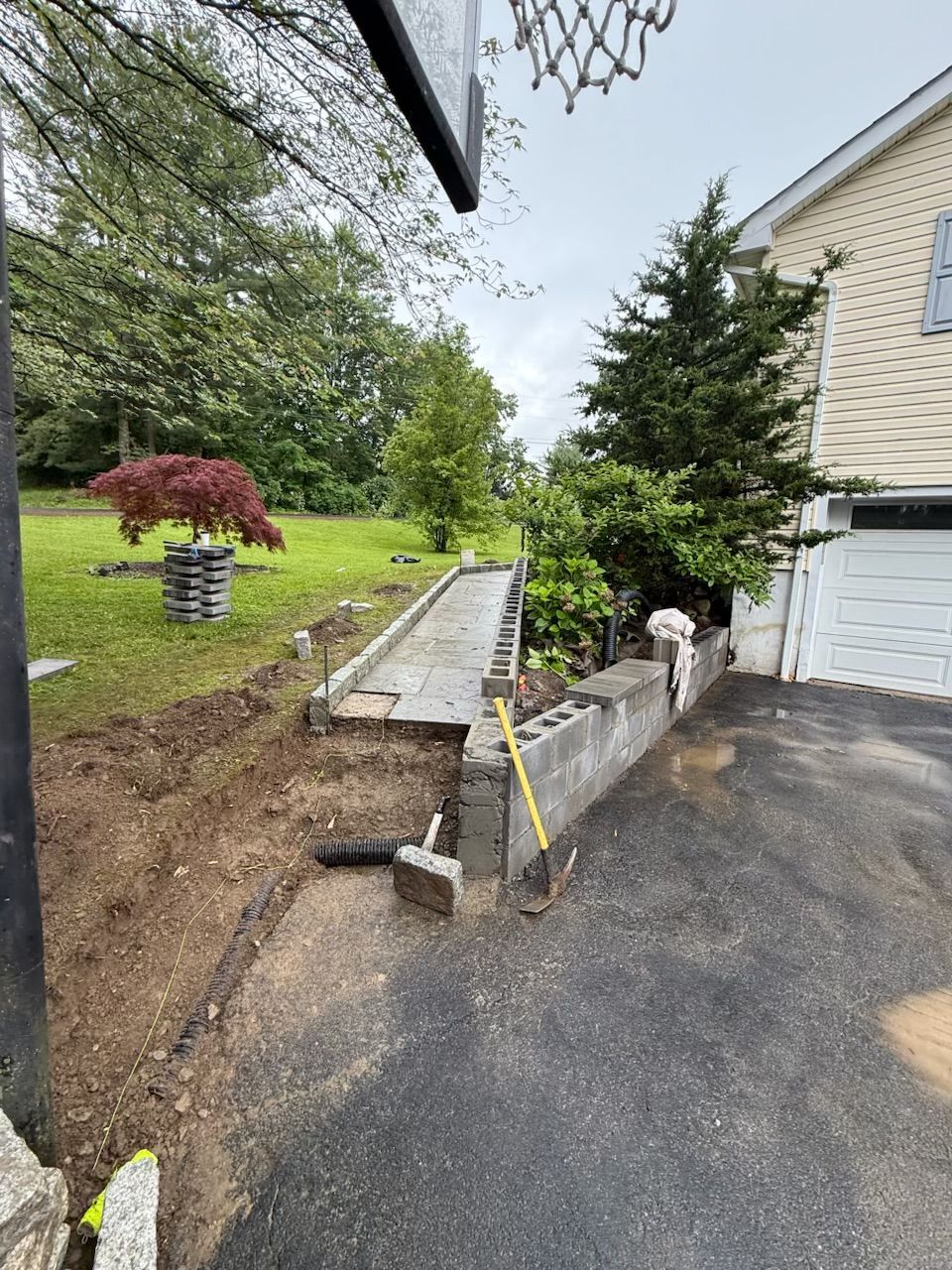Asphalt driveway with concrete retaining wall, soil excavation, and landscaping near a house.