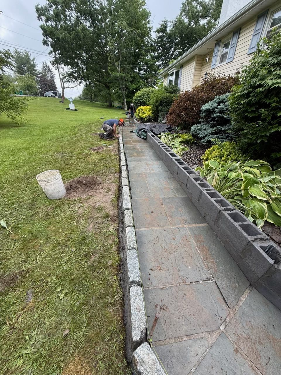 Pathway bordered with stone and concrete blocks, beside a lawn and house with landscaping.