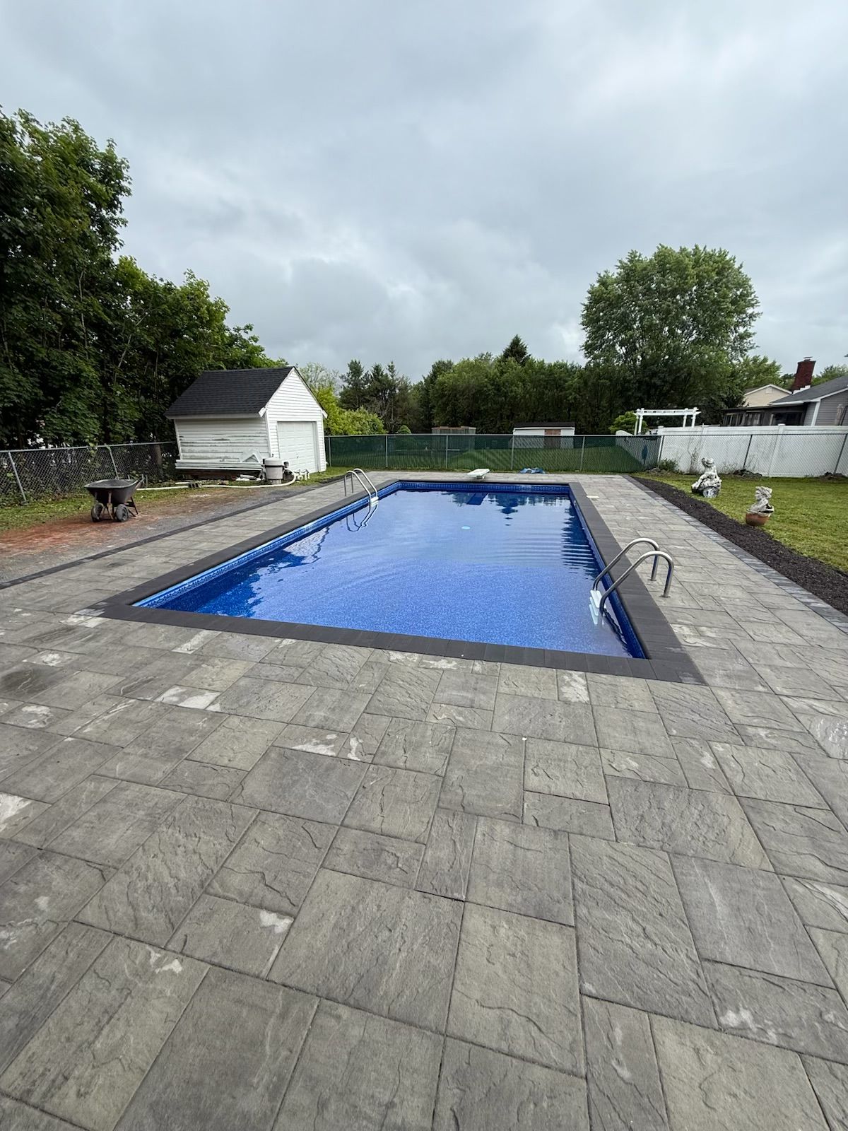Rectangular pool with blue water and dark coping surrounded by gray pavers on a cloudy day.