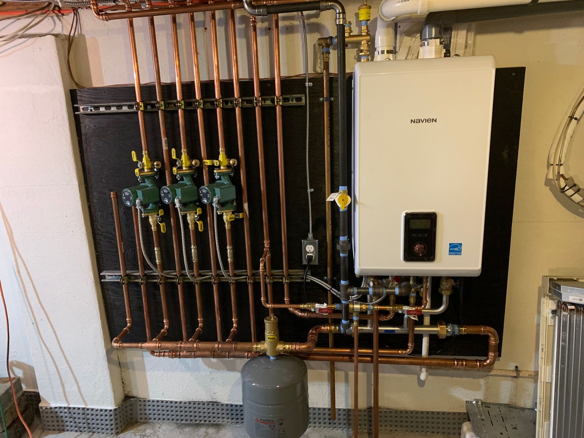 Copper pipes and a boiler system mounted on a wall in a basement.