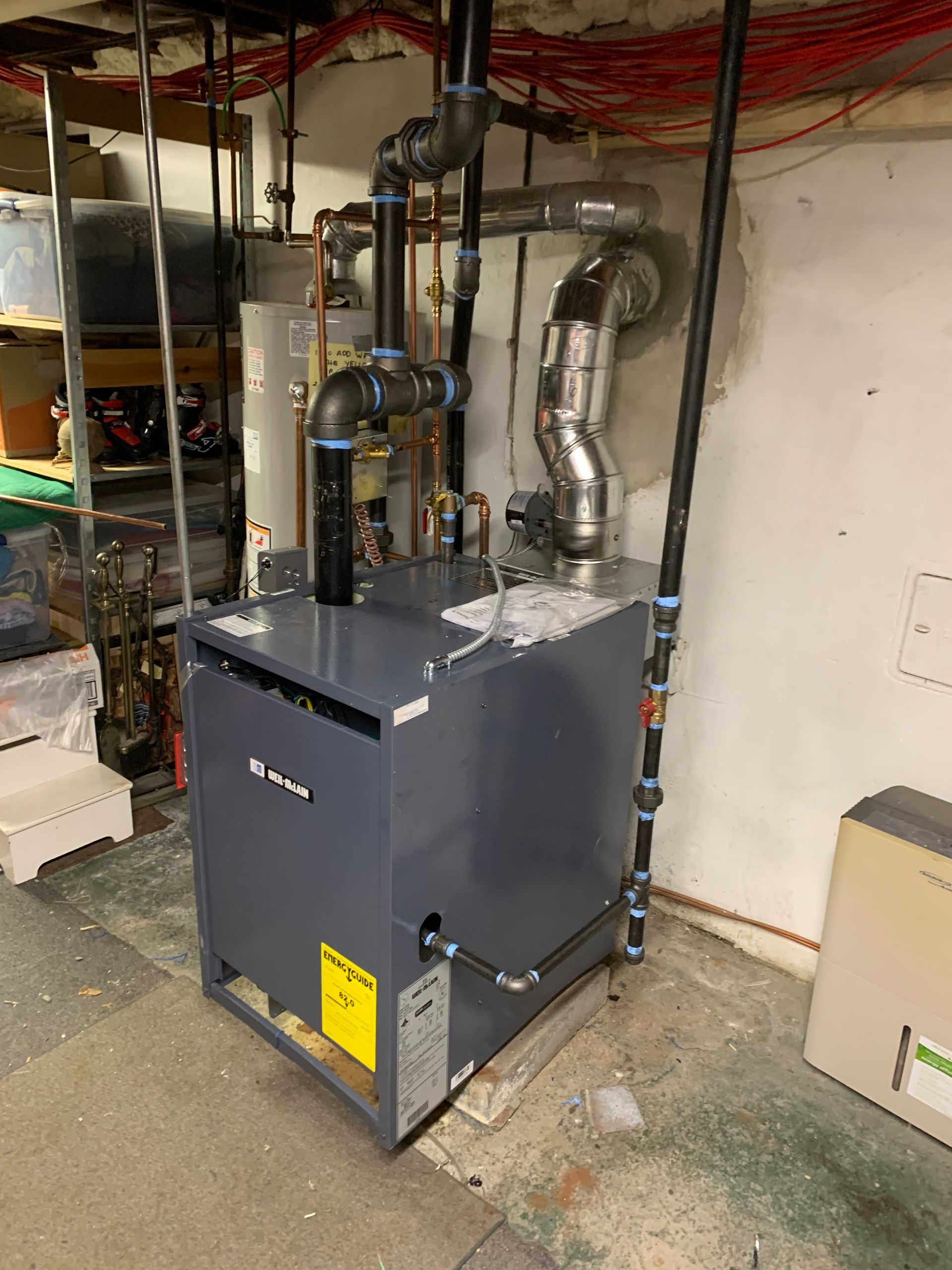 A furnace with black and gray pipes in a basement setting.