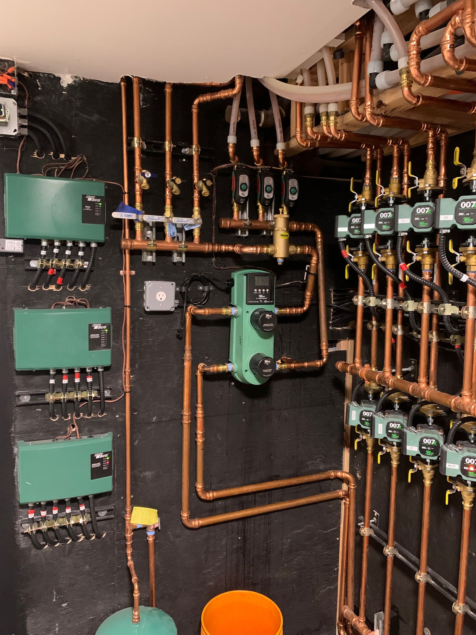 Complex copper plumbing system with green control panels against a dark wall.