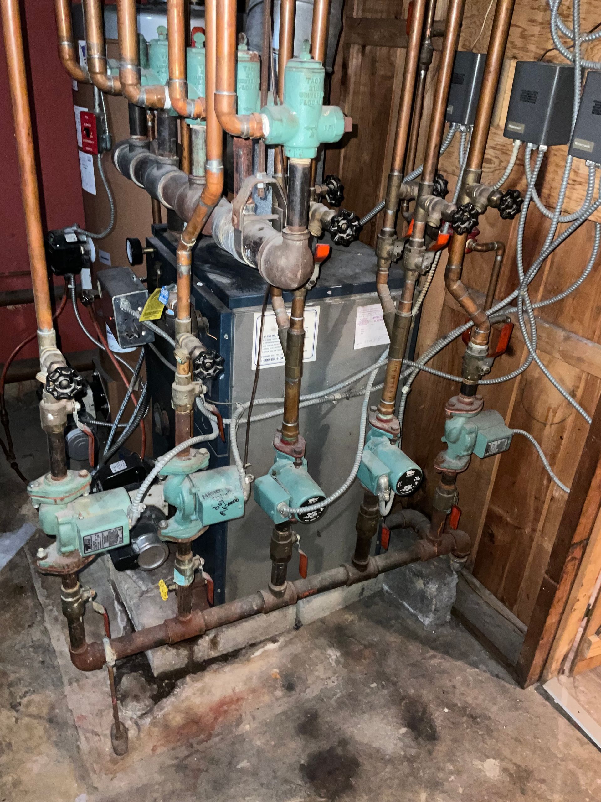 Copper pipes and heating equipment in a utility room. Pumps, valves, and wiring are visible.