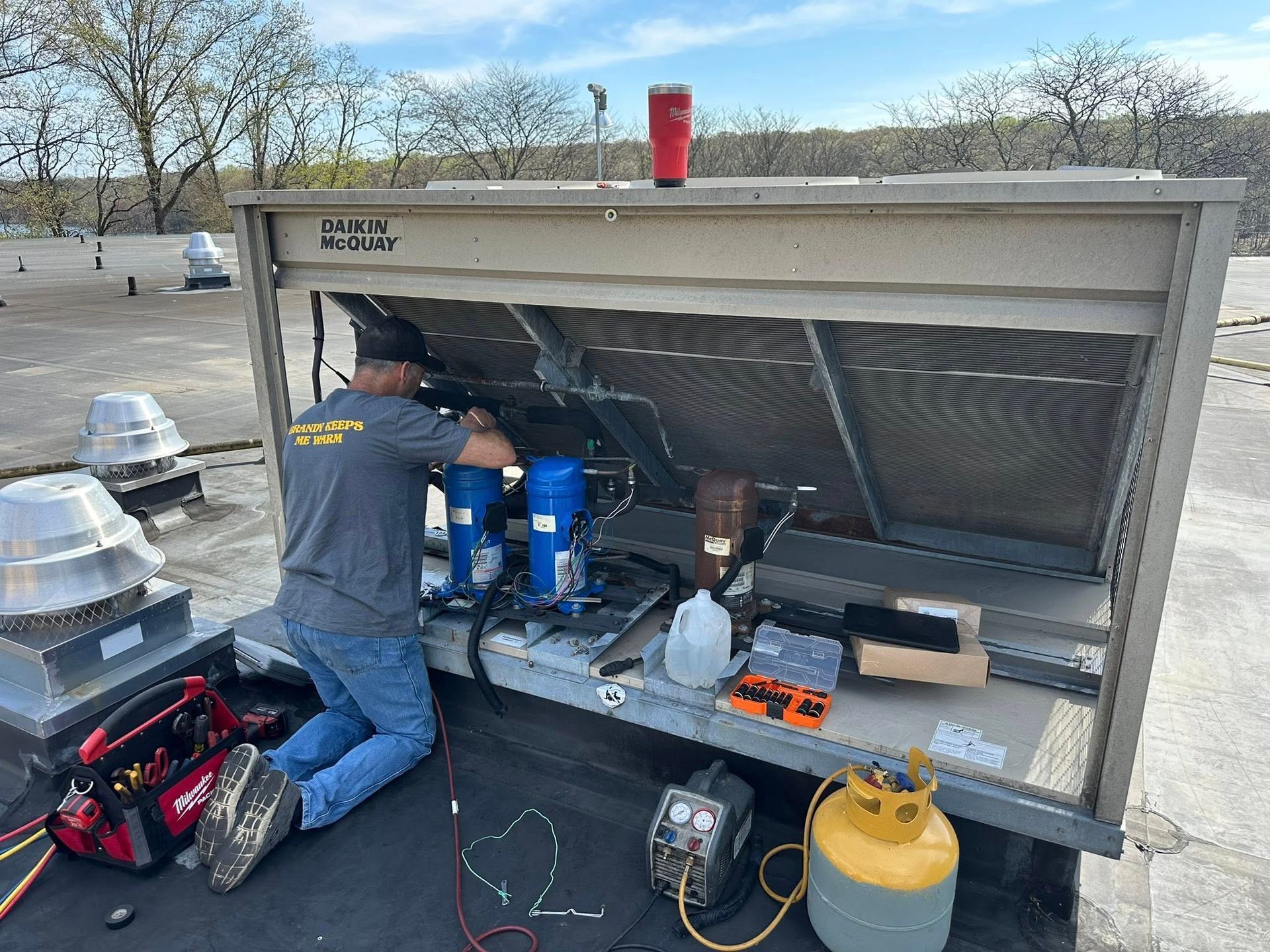 HVAC technician working on rooftop unit. Equipment and tools visible, sunny day.
