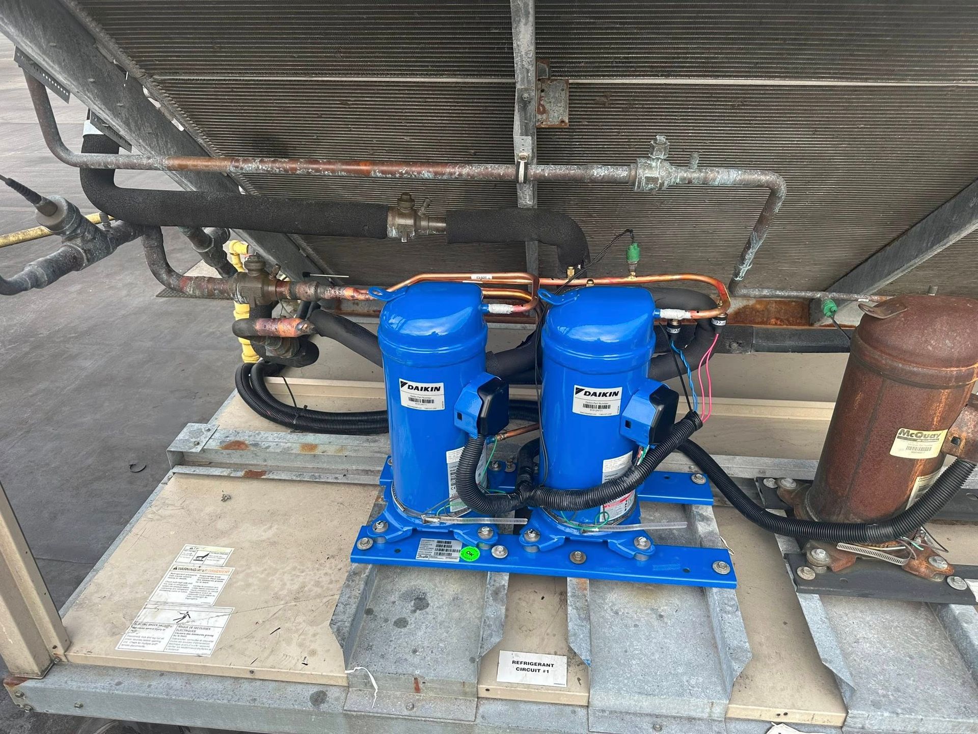 Two blue air conditioning compressors on a rooftop unit, with copper pipes and a brown tank.