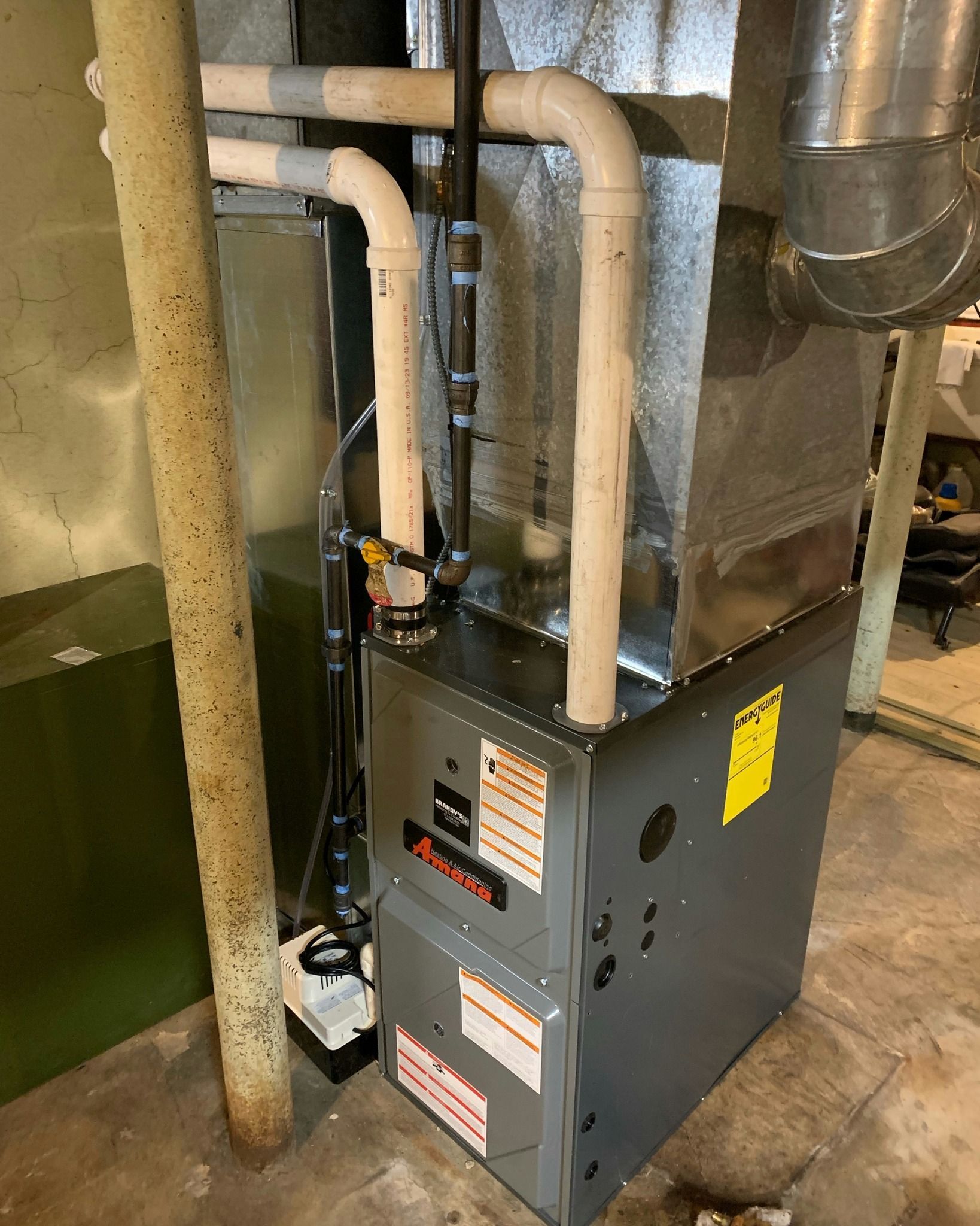 Furnace in a basement. Ductwork and piping visible, with a yellow energy guide label.
