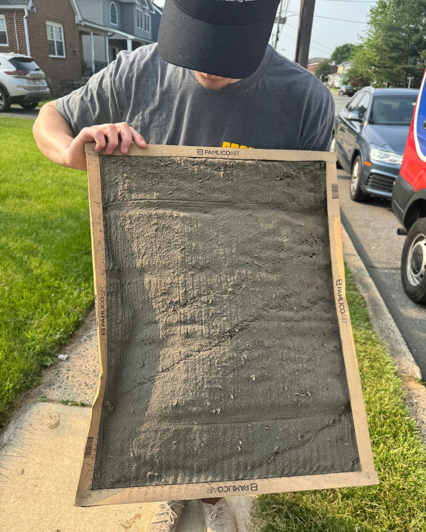Person holding a framed, rectangular sample of gray concrete outdoors, along a sidewalk.